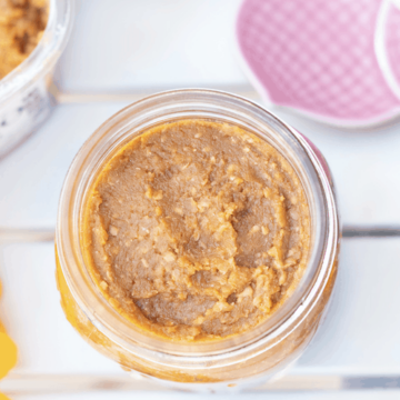 A close-up of a jar has become a miso pickling bed for garlic. White miso has been piled right to the top.