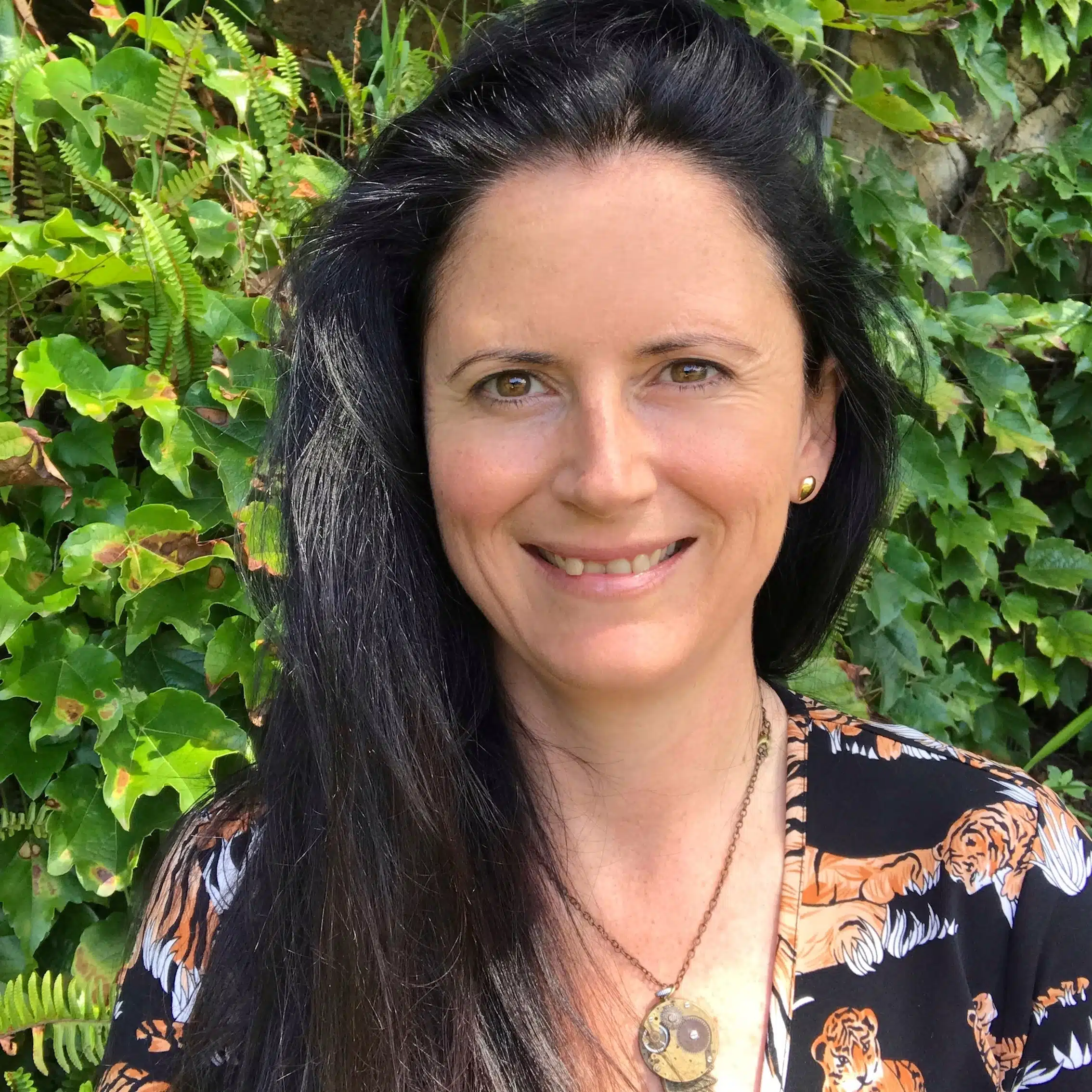 About page photo showing a portrait photo of a smiling white woman with long black hair wearing a tiger print dress.