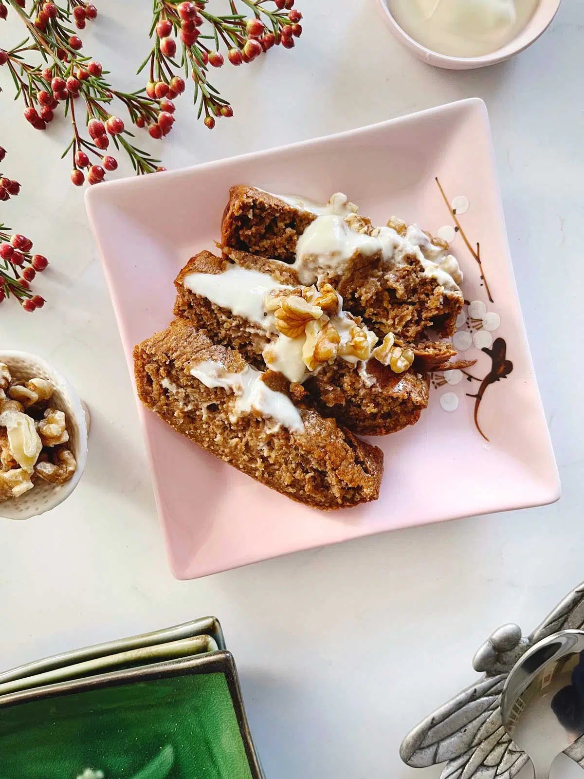 A small pink plate is filled with slices of baked oats drizzled with yoghurt and topped with walnuts.