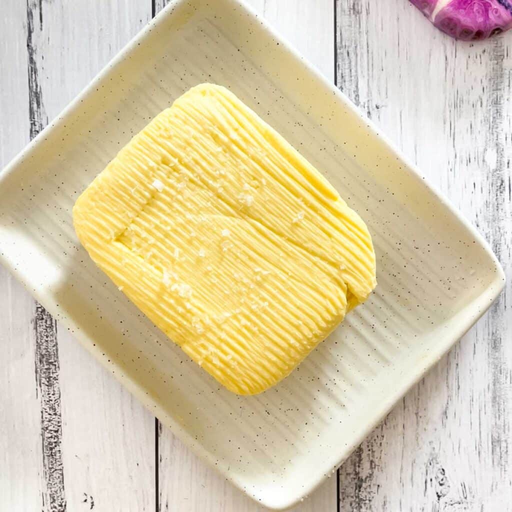 A block of yellow cultured butter sprinkled with sea salt is sitting in a ceramic butter dish.