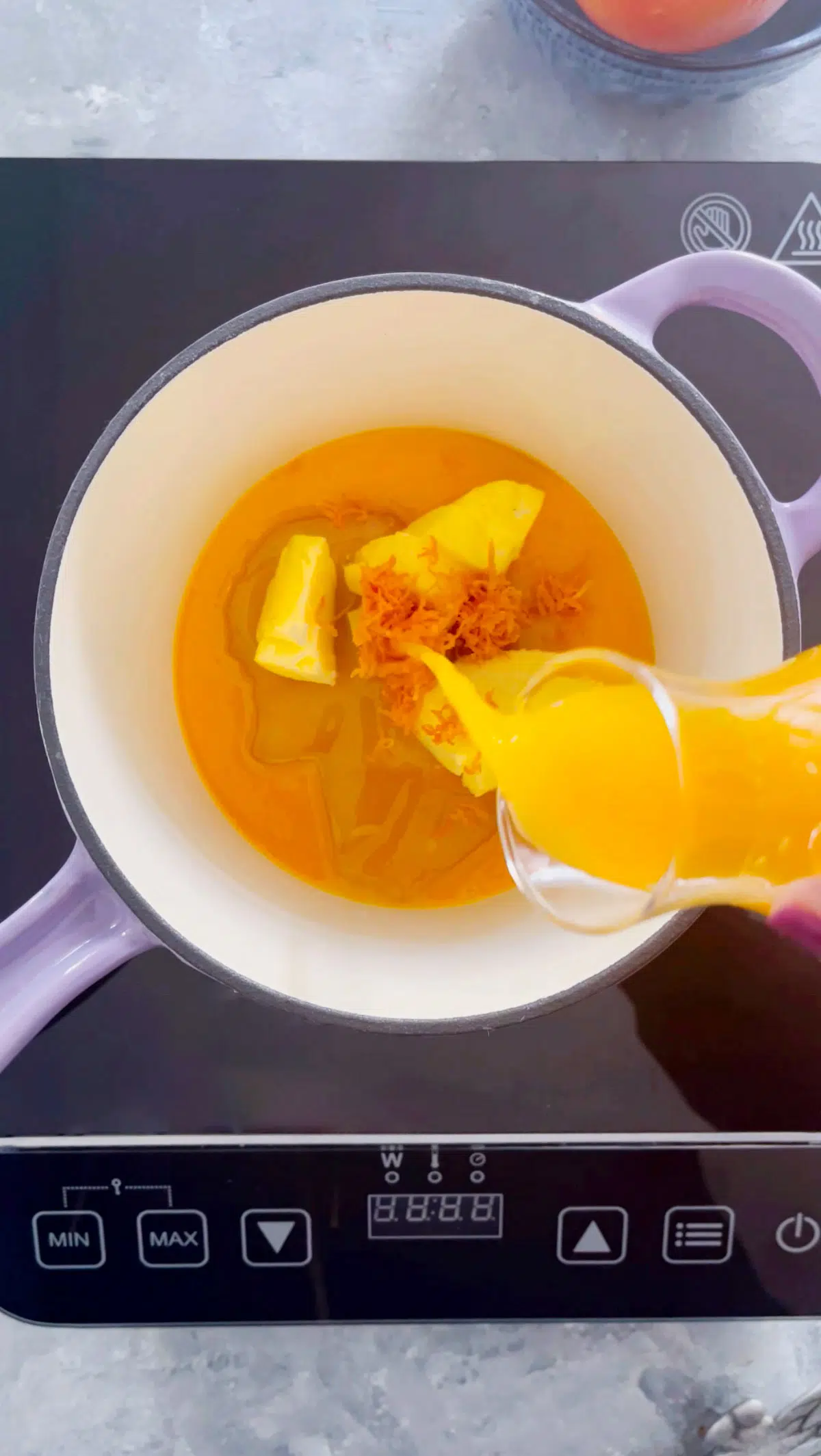 A small purple saucepan is sitting on top of an induction with the bright orange tangelo curd warming inside it.