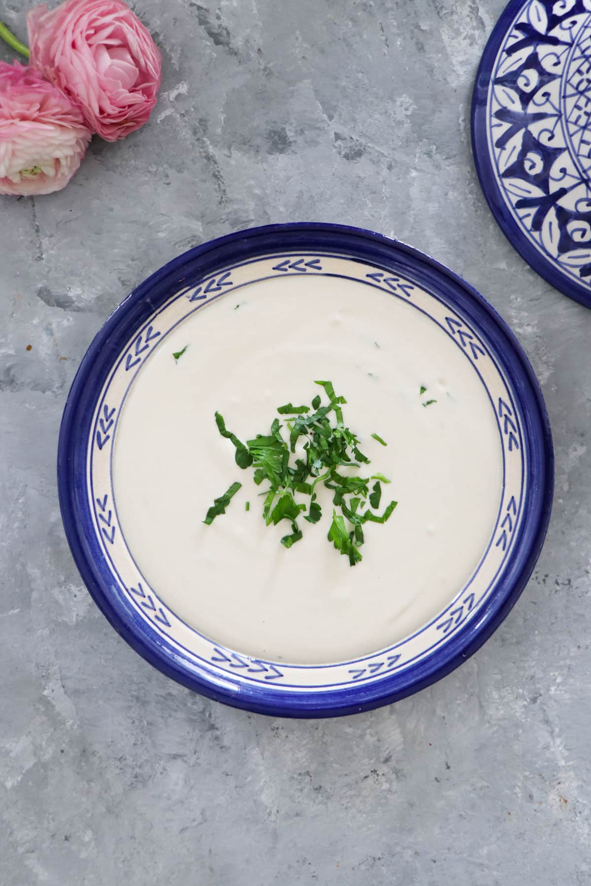 The base of a blue and white patterned Moroccan tagine if filled with creamy lemon tahini sauce.