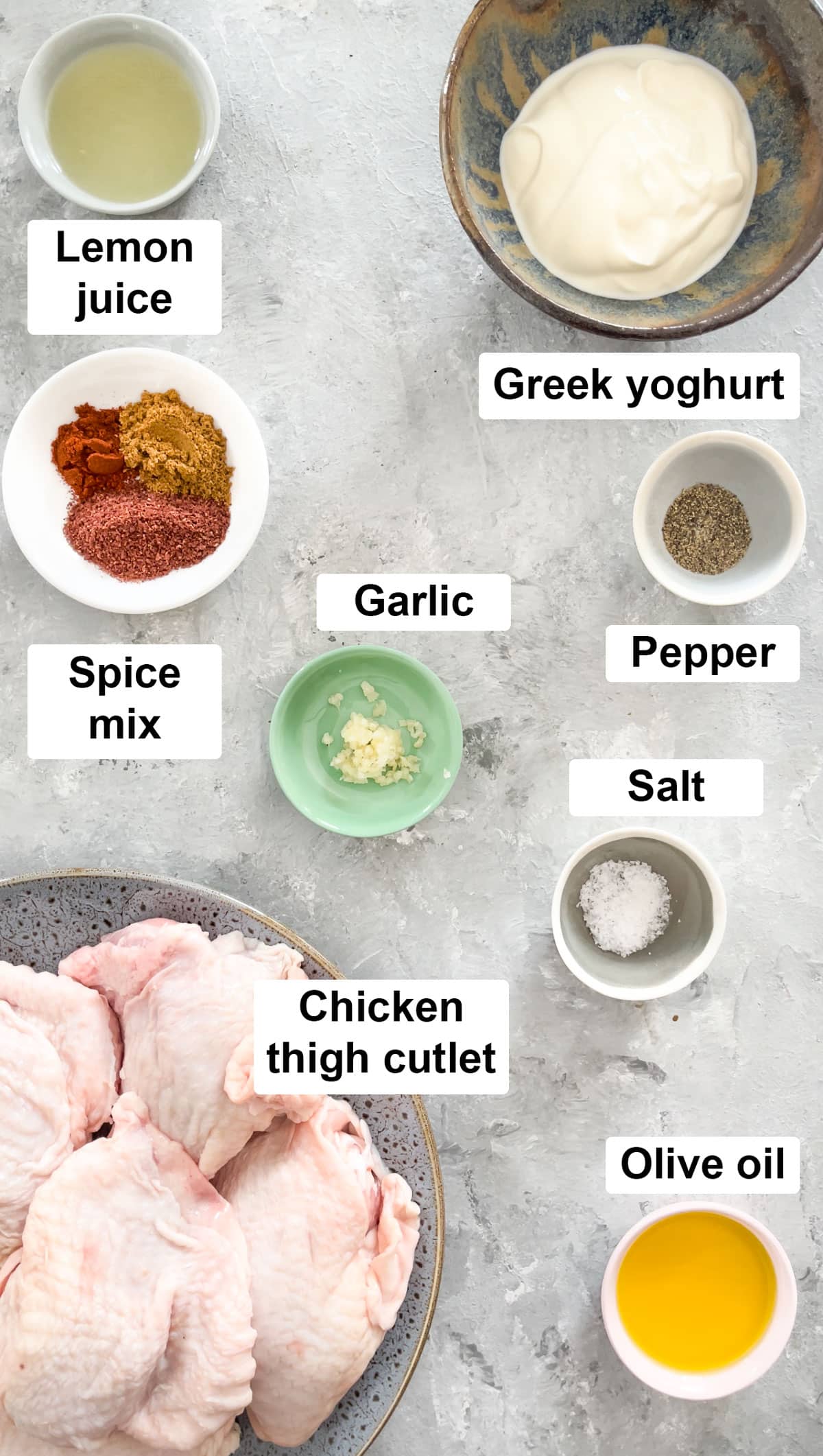 All the ingredients needed to make yogurt marinated chicken have been laid out across a table in bowls.