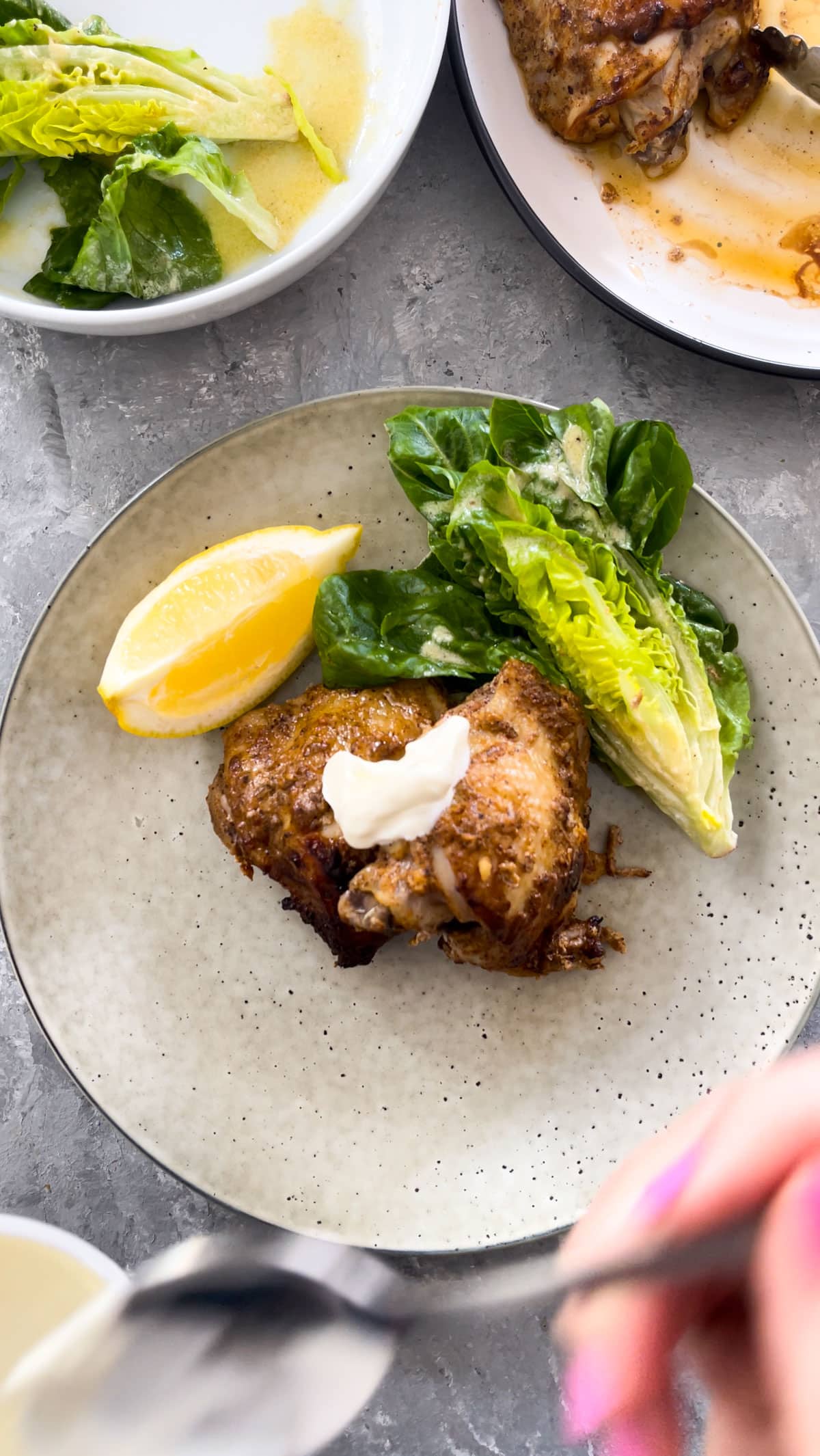 A plate of Yogurt Marinated Chicken and salad is surrounded by more plates of salad and chicken to the side of the dish.
