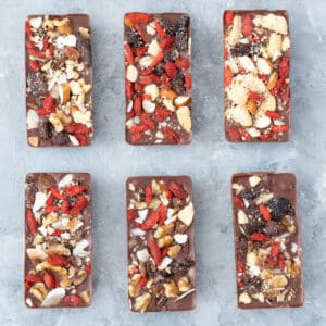This is a square image showing six homemade chocolate bars all decorated and sitting on a grey table in two rows of three.