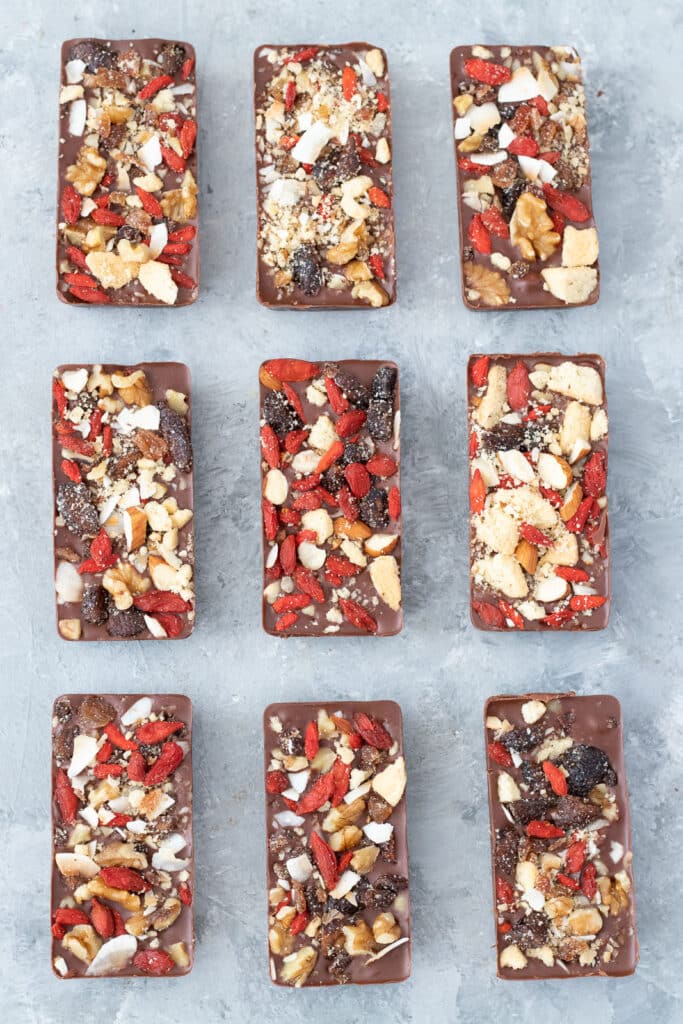 Nine homemade chocolate bars are all decorated and sitting on a grey table in three rows of three.