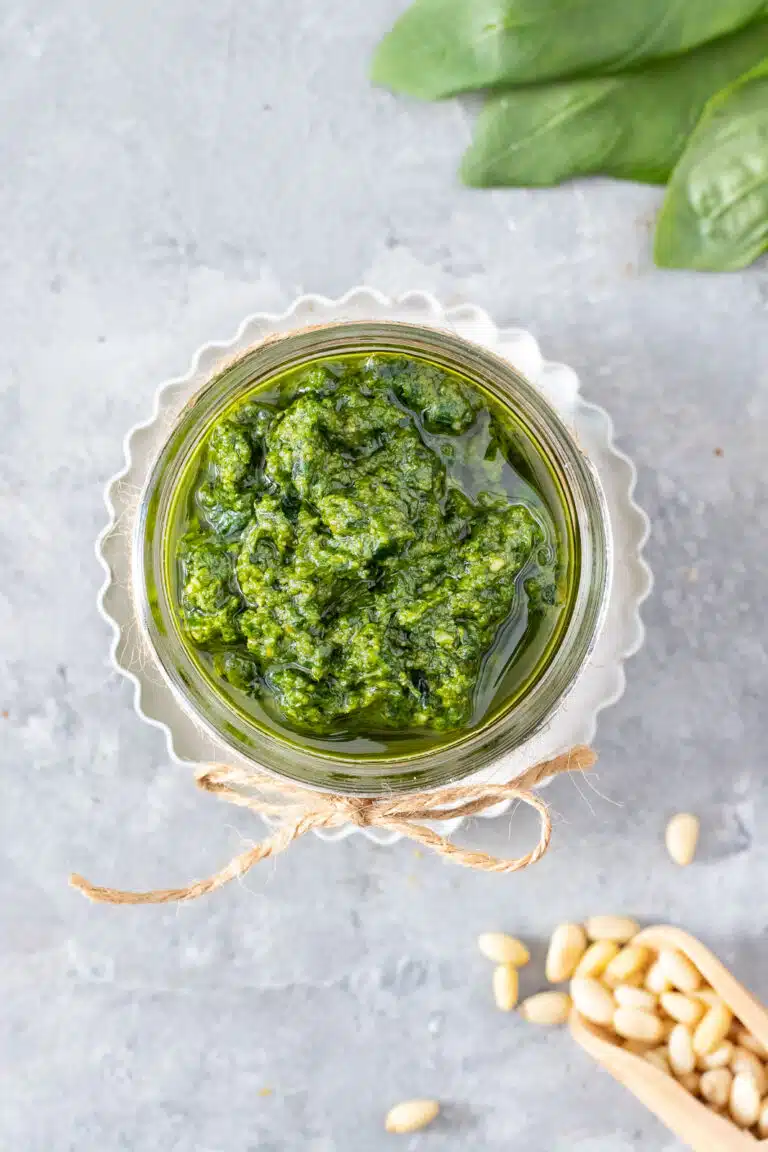 A small jar with a bow tied in brown string around the rim is filled with bright green dairy free pesto.
