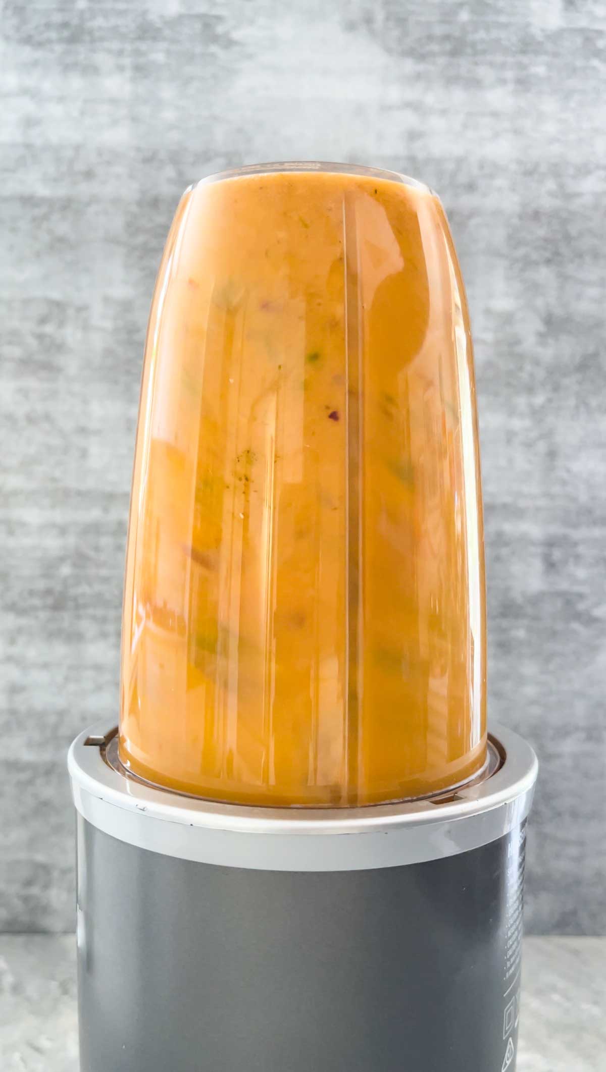 Bright orange mango chilli hot sauce is being pulverised in a small blender.