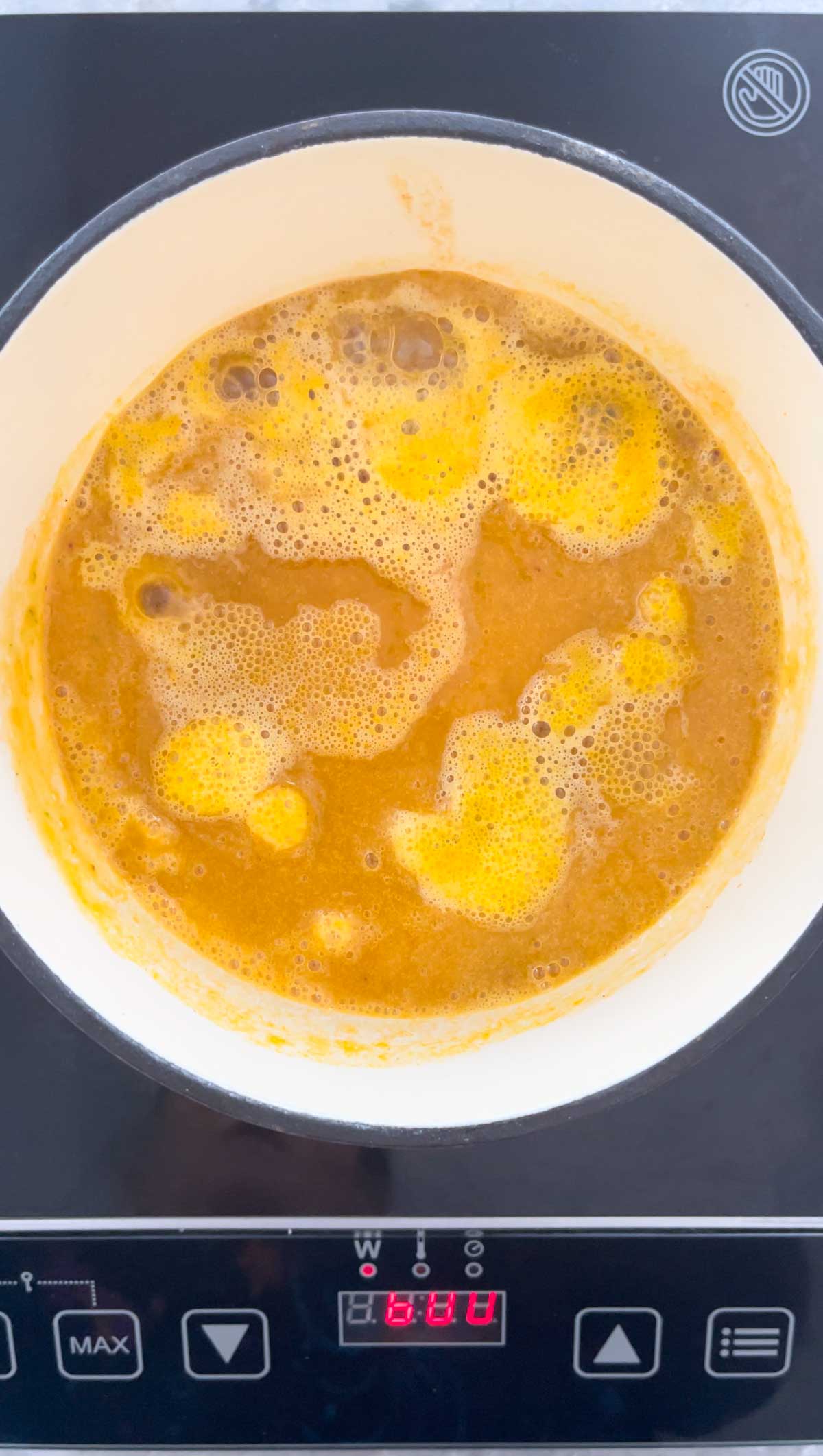Mango chilli sauce being simmered in a small ceramic saucepan on an induction stove top.