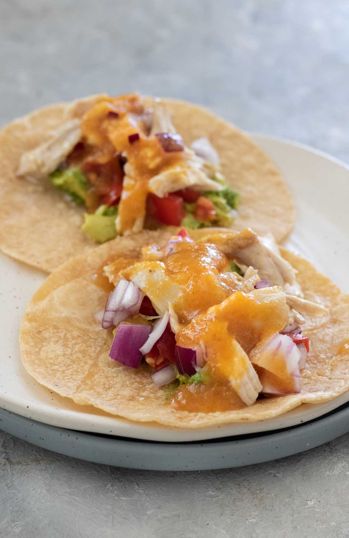 Close-up of two chicken and vegetable tacos topped with bright orange mango chilli hot sauce.