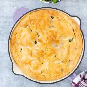 An overhead image of a golden skillet spanakopita sitting on a grey table.