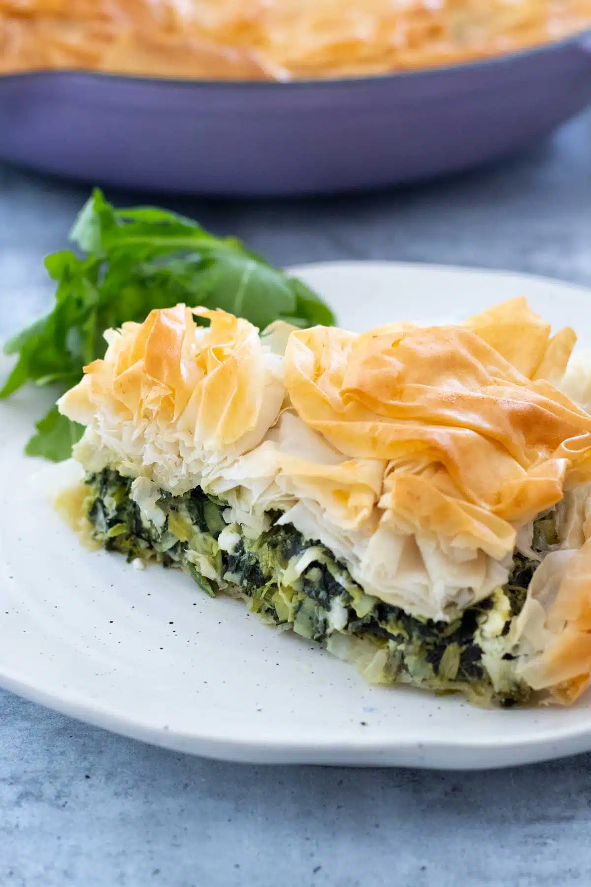 A piece of spanakopita has been cut and put on a white speckled plate with some rocket.