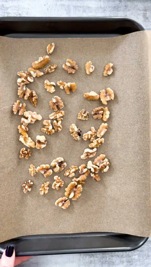 A small baking tray lined with baking paper has walnuts spread across ready to go in the oven for toasting.