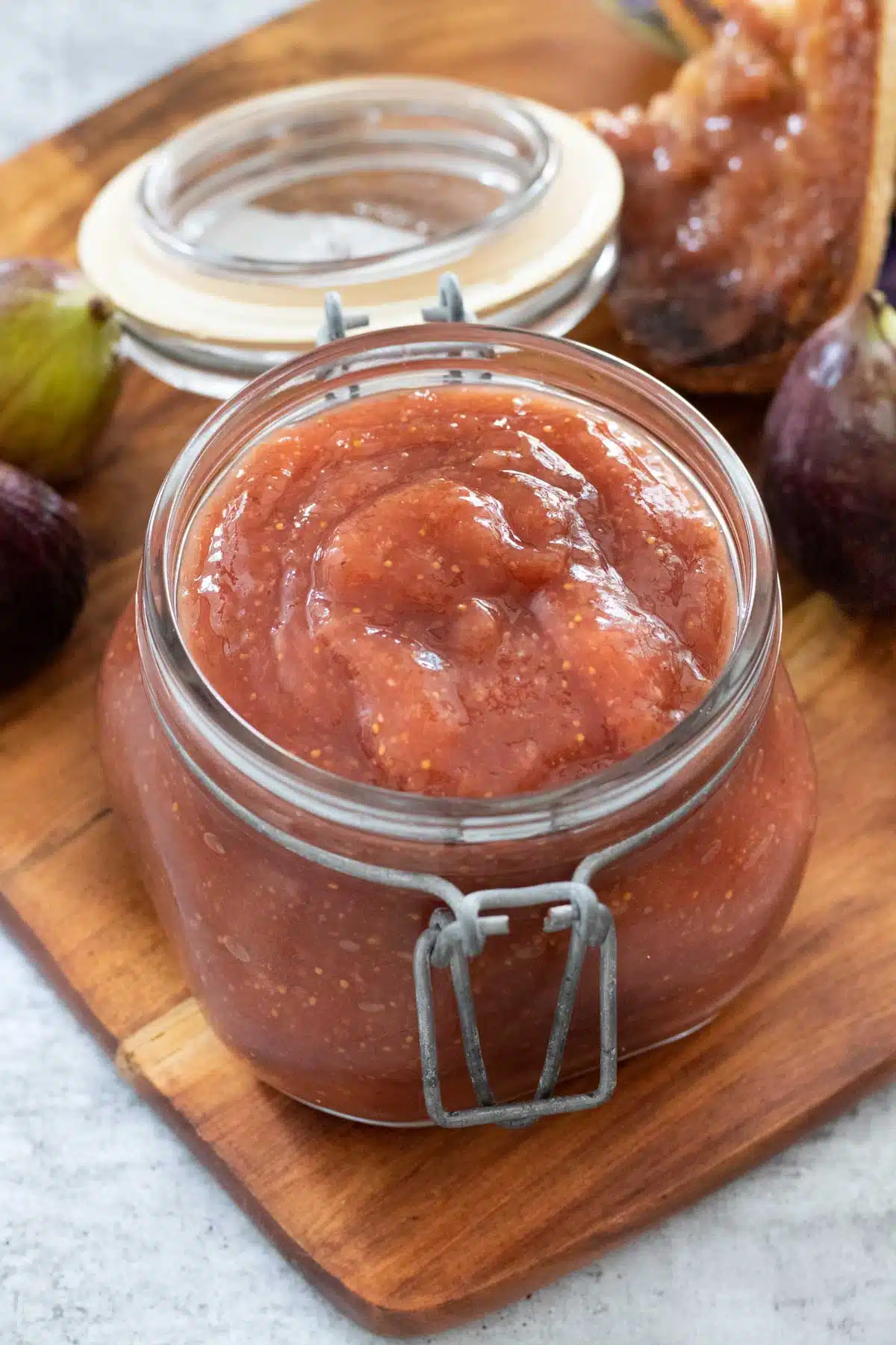 A jar with flip top lid has been filled with fermented fig butter. It's sitting on a wooden serving board with some figs and toast behind it.