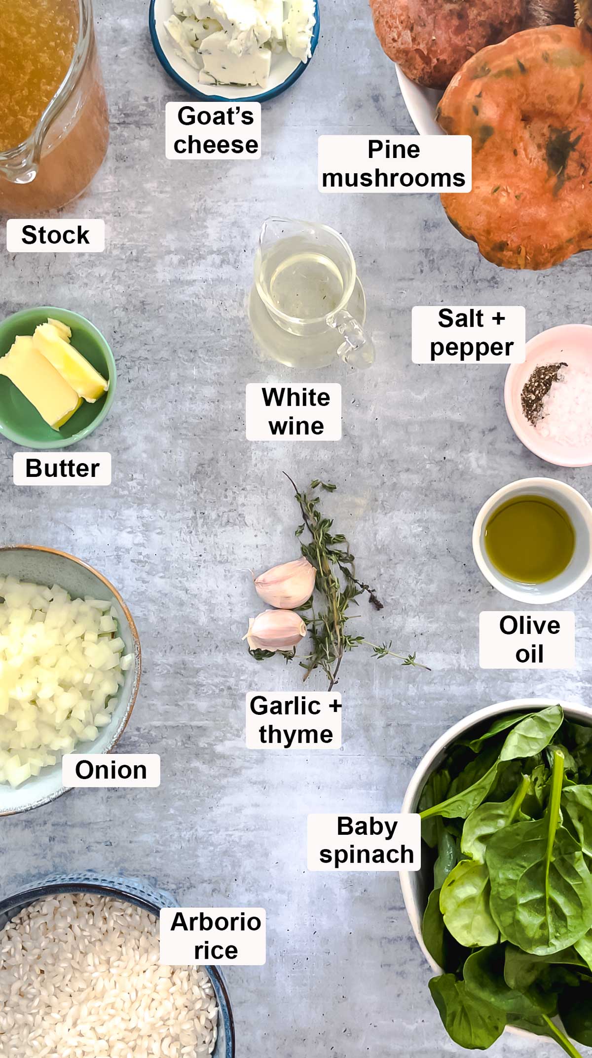 All the ingredients needed to make pine mushroom risotto have been laid out across a grey table in small bowls.