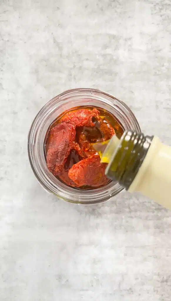 Pouring olive oil over a jar of oven dried tomatoes