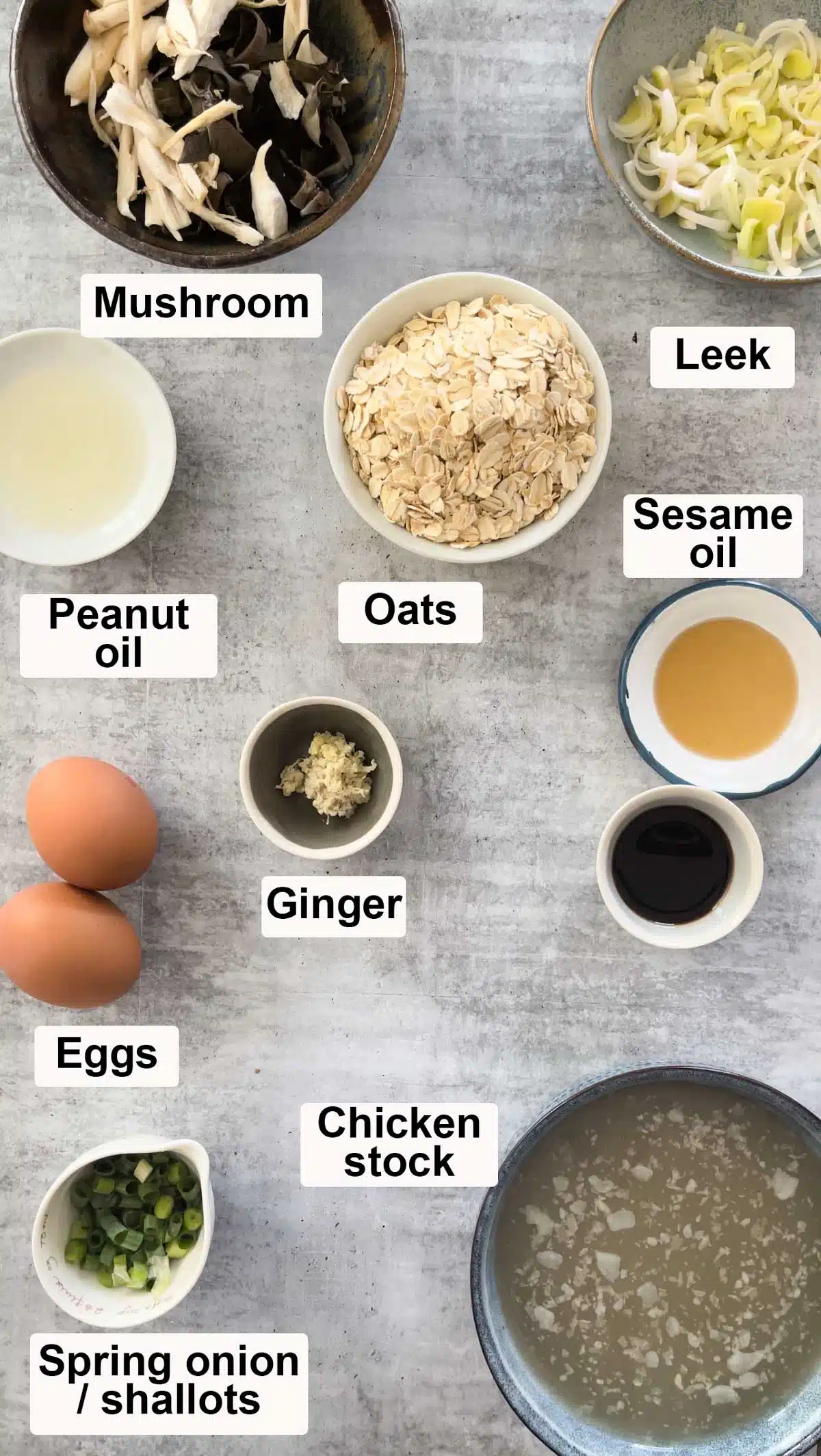 All the ingredients needed to make savoury oats have been laid out in various bowls across a grey table.