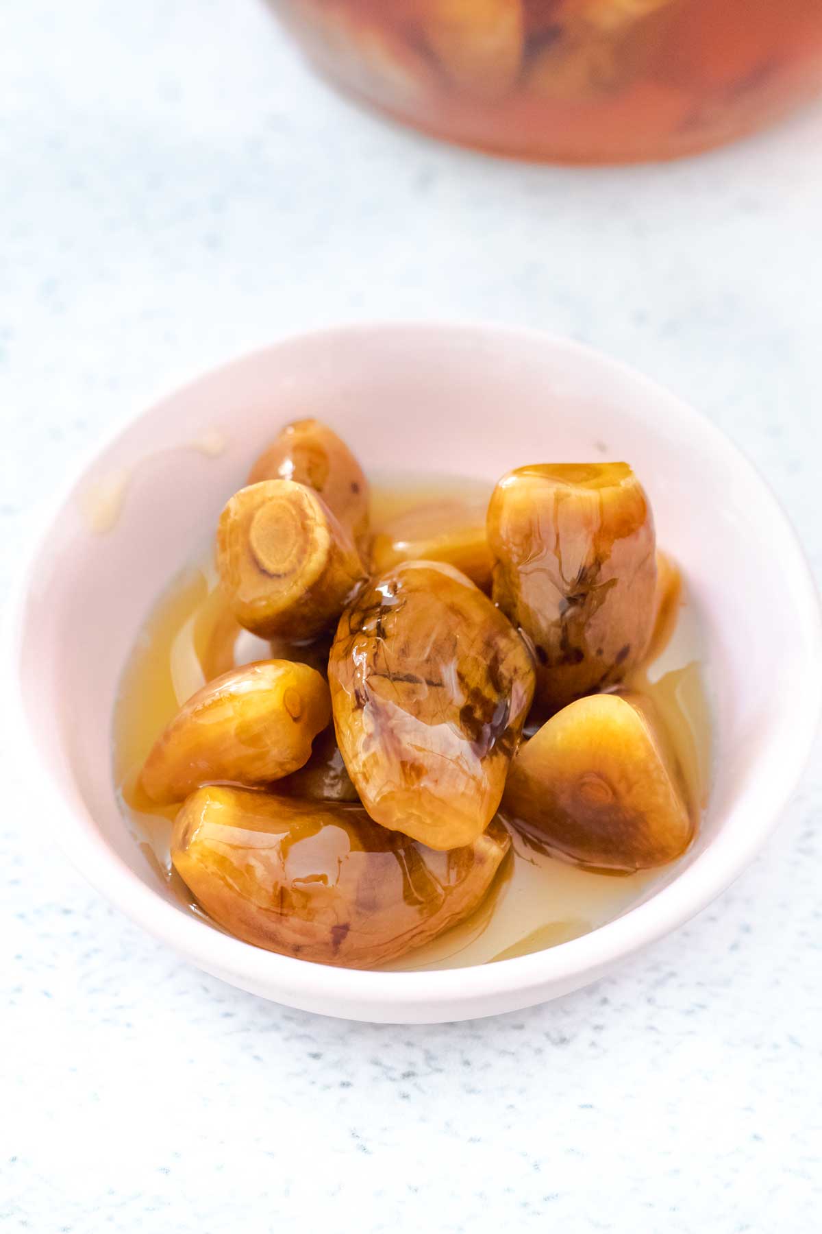 A small pink bowl has several garlic cloves in it that have been fermented and aged in honey.