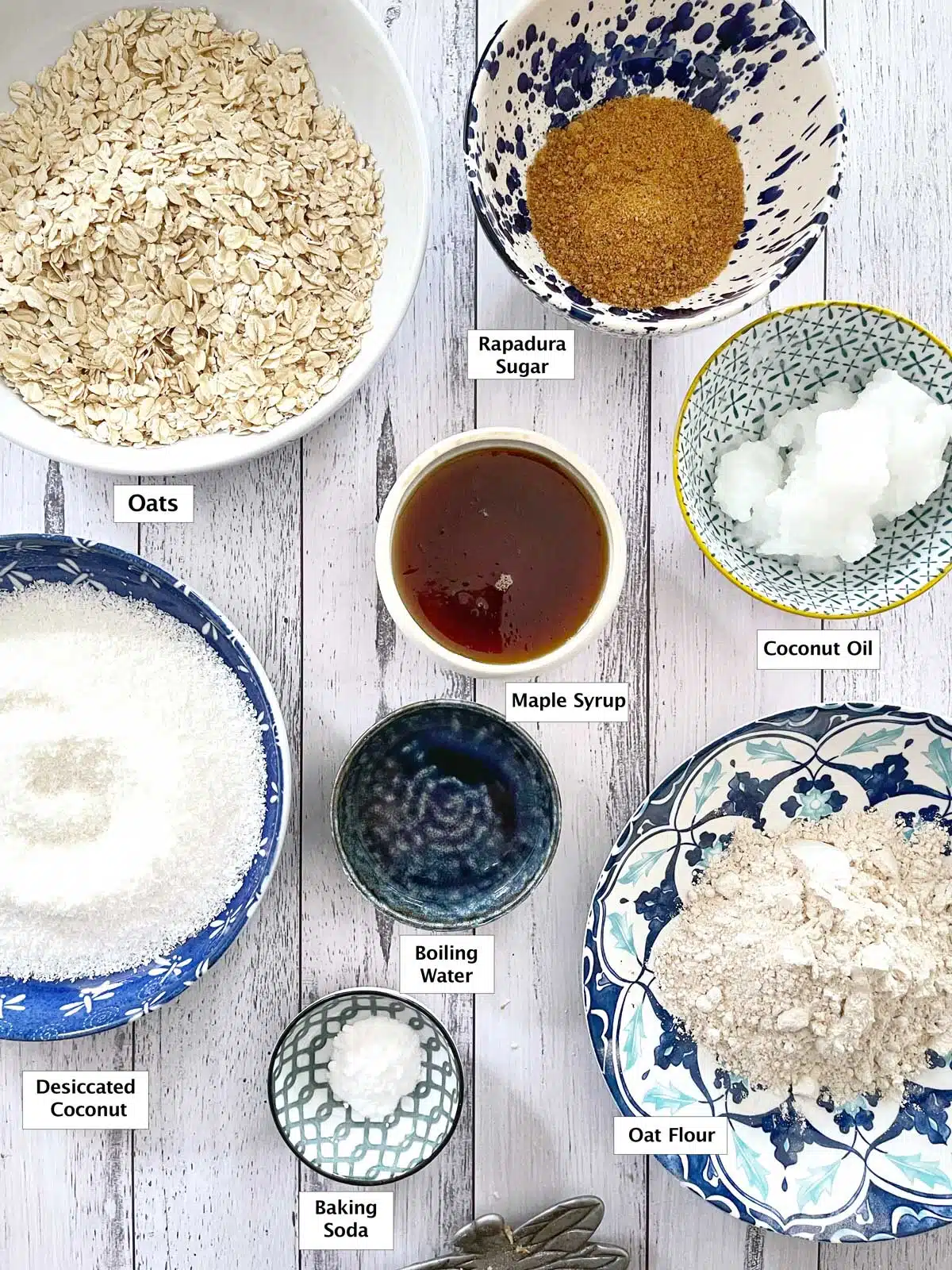 All the ingredients needed to make Anzac biscuits are laid out across a table in small bowls.