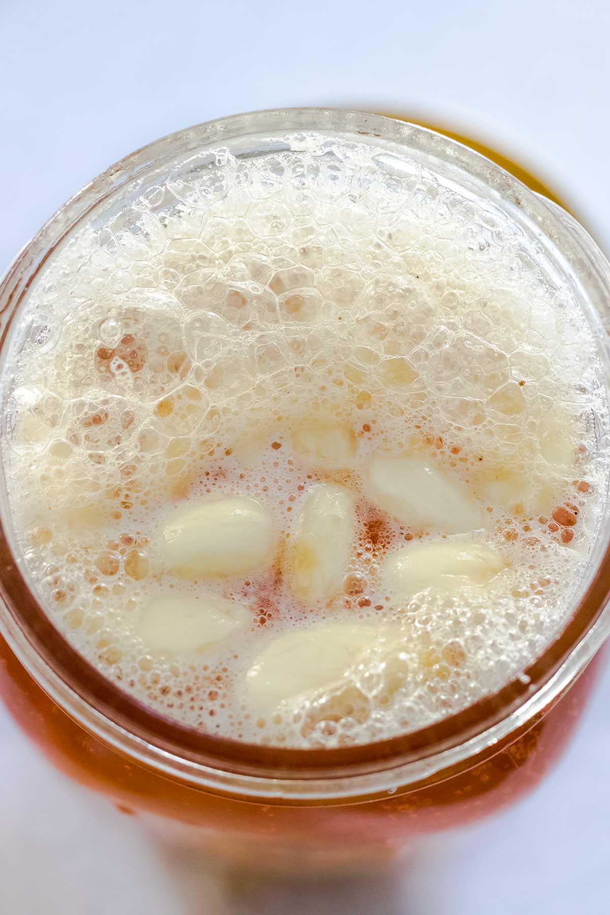 Looking into a jar filled with honey and garlic cloves that are bubbling due to fermentation.