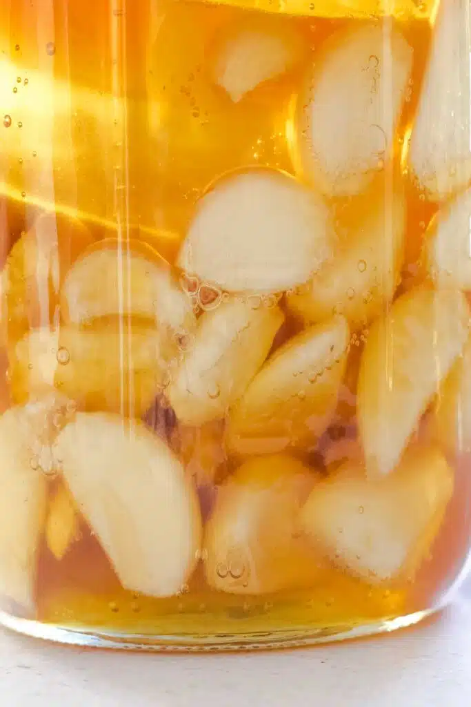 Garlic cloves in the bottom of a jar are submerged under honey.