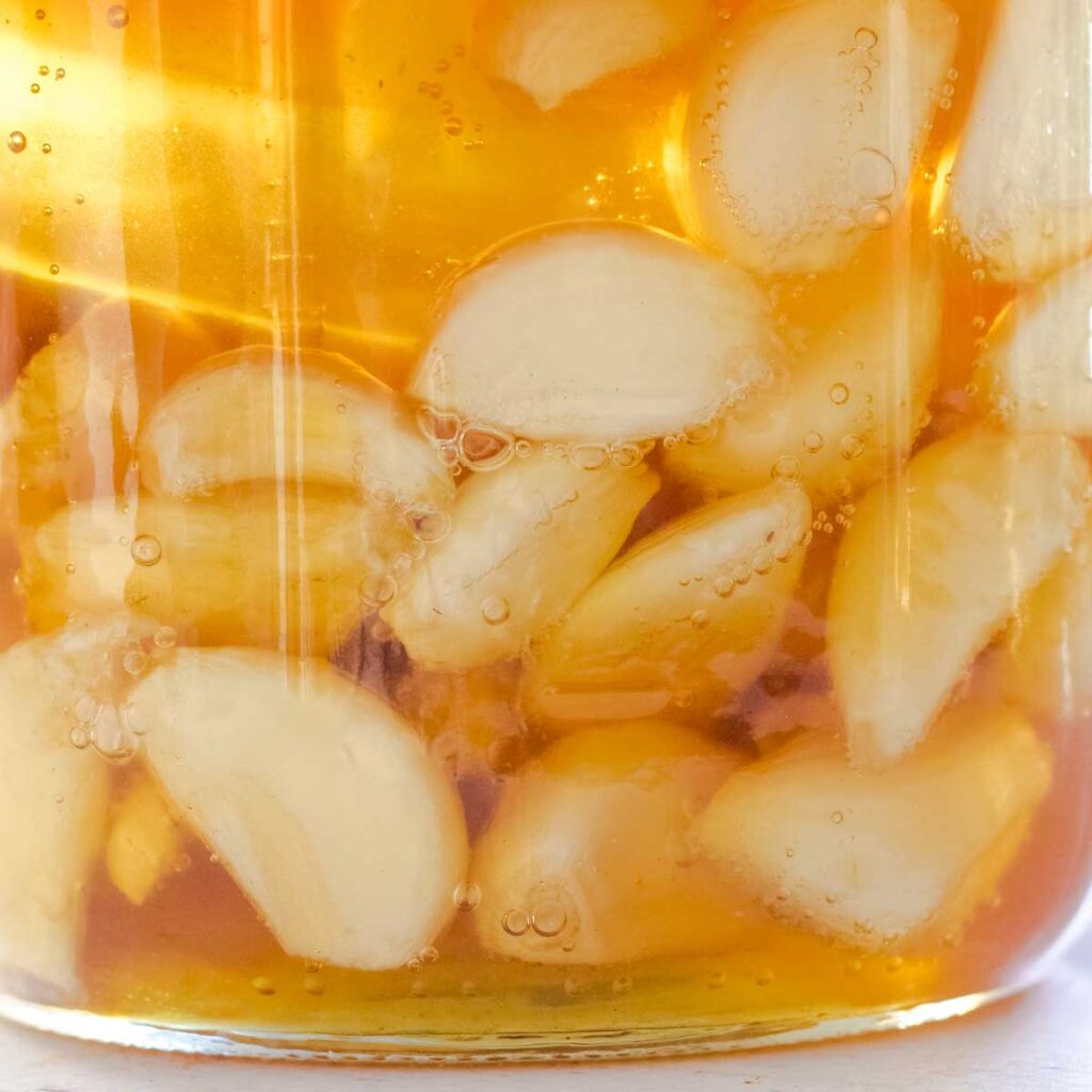 Garlic cloves surrounded by small bubbles are submerged in honey in the bottom of a jar.