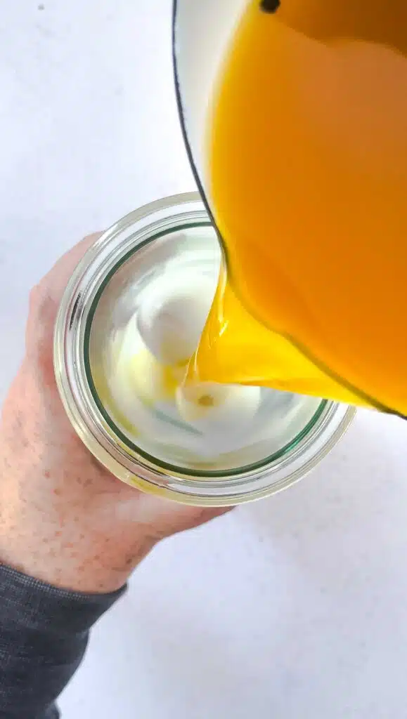 Yellow pickling juice is being poured into a jar with hard boiled eggs.