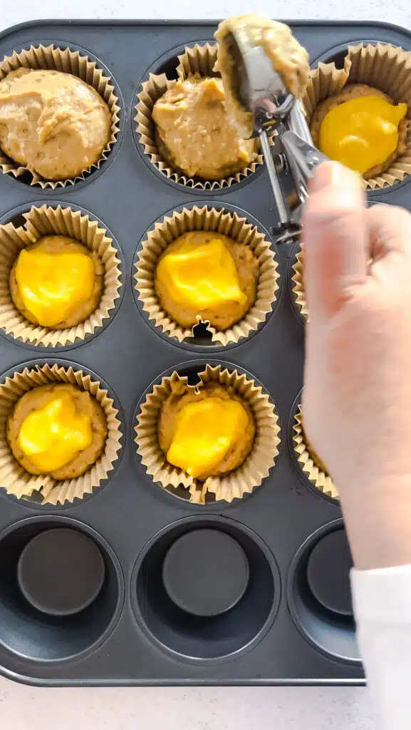 Adding muffin batter over the top of the lemon curd.