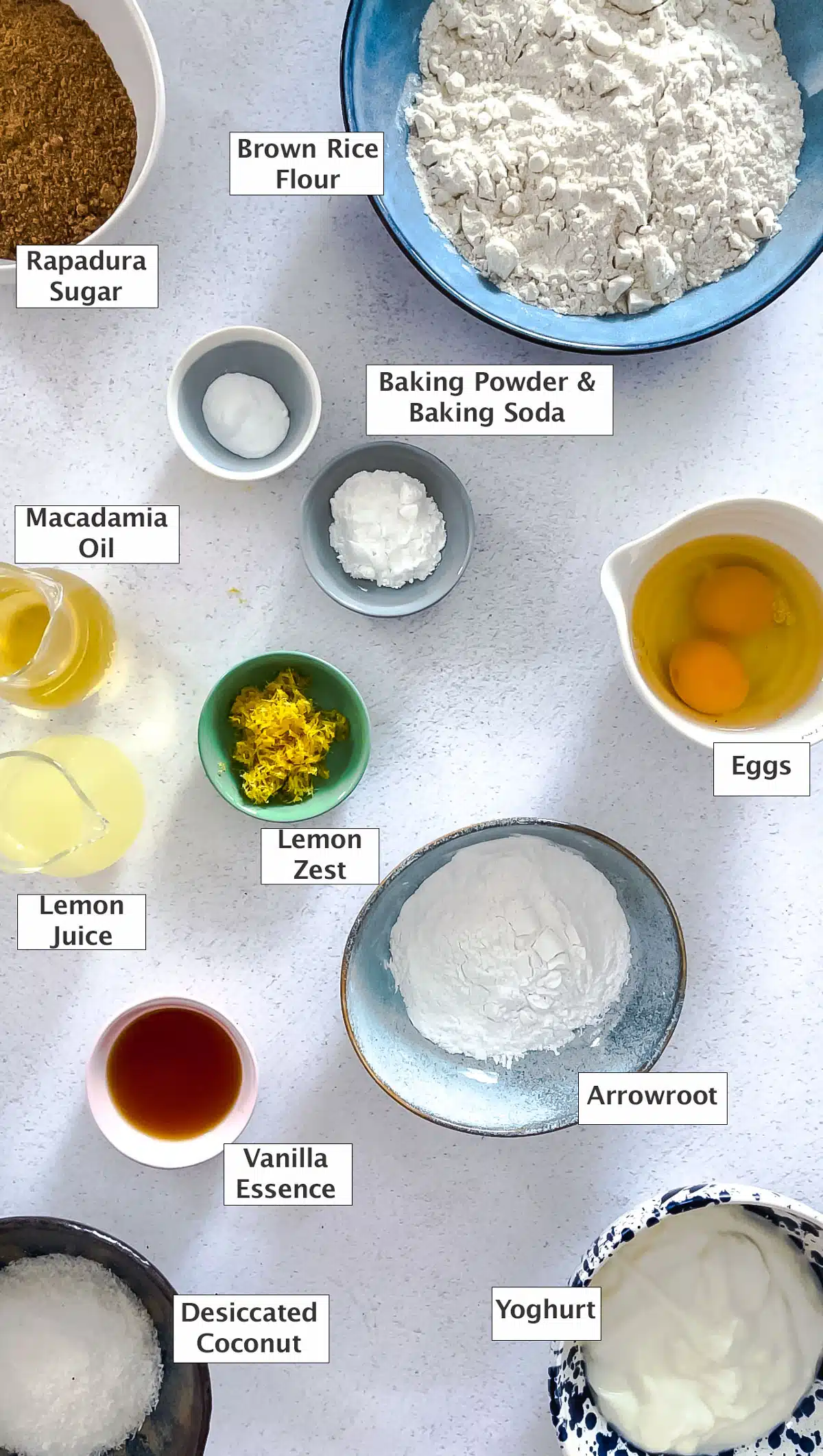 All the ingredients needed to make lemon curd muffins have been laid out across a table in various small bowls.