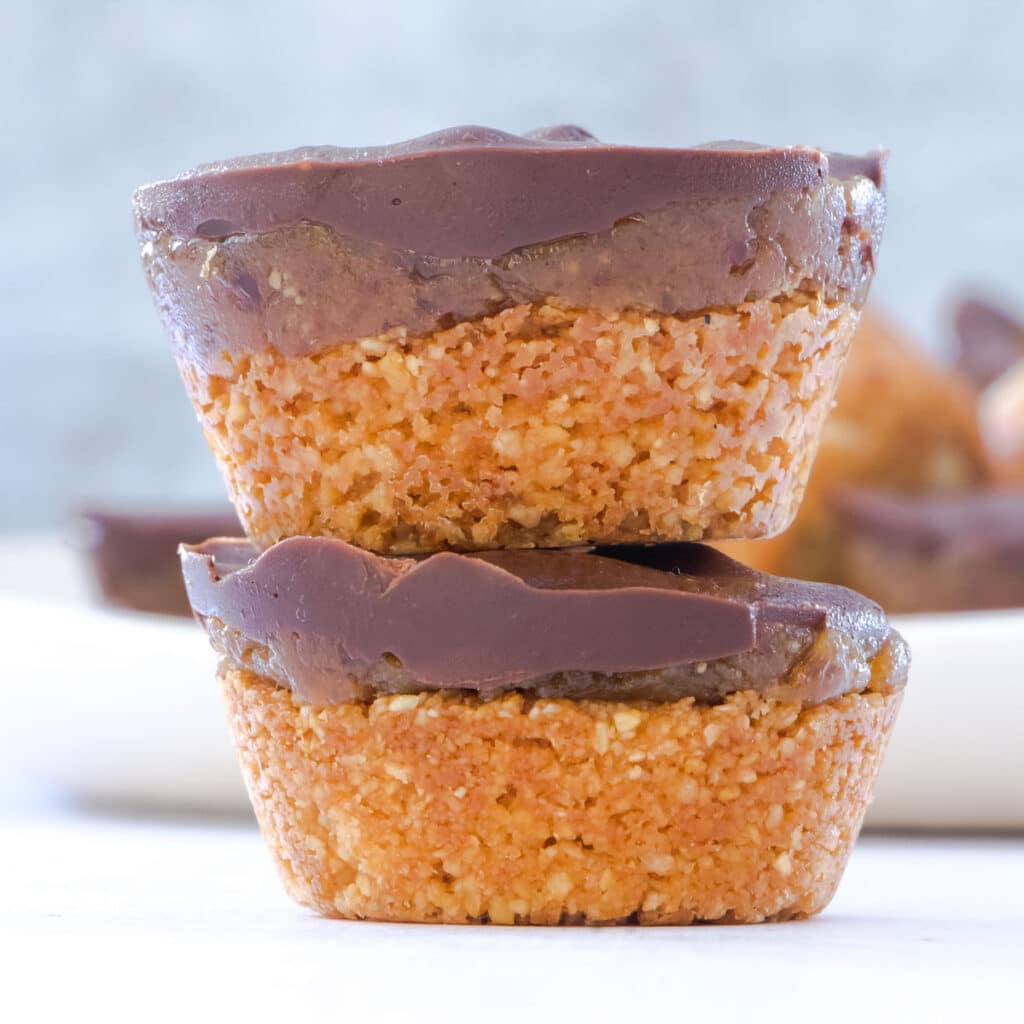 Two Twix cups stacked on top of each other. A white plate with more Twix cups can be seen in the background.