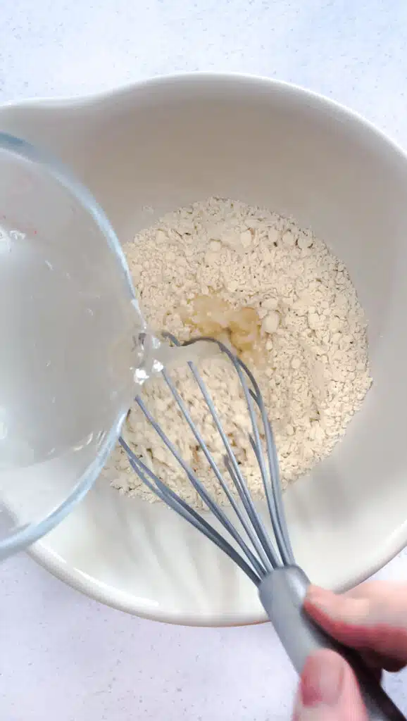 Water is being whisked into chickpea flour in a large cream-coloured bowl.