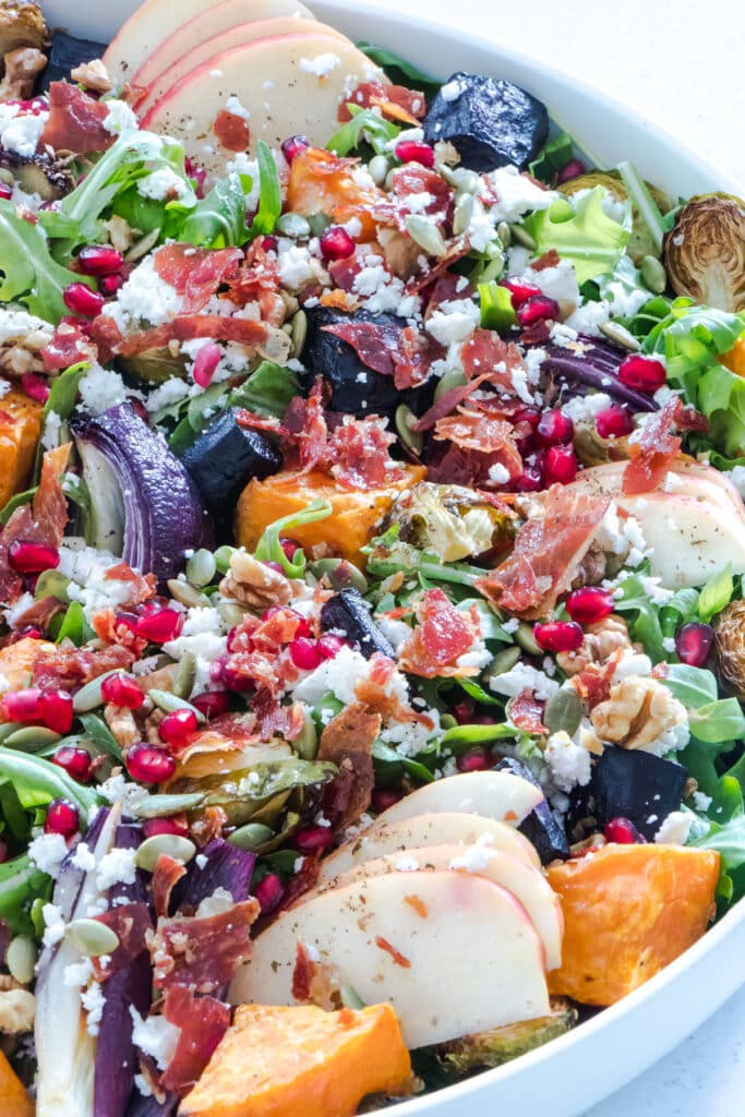 Close-up of brightly coloured Autumn Harvest Salad in a white bowl with vegetables, nuts, prosciutto, feta and apple.