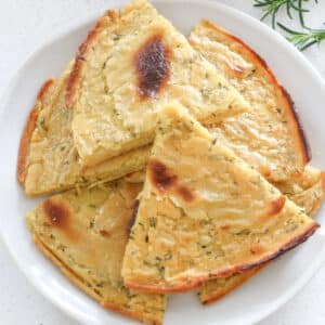 Triangular slices of chickpea flatbread are arranged in a circle on a white plate.