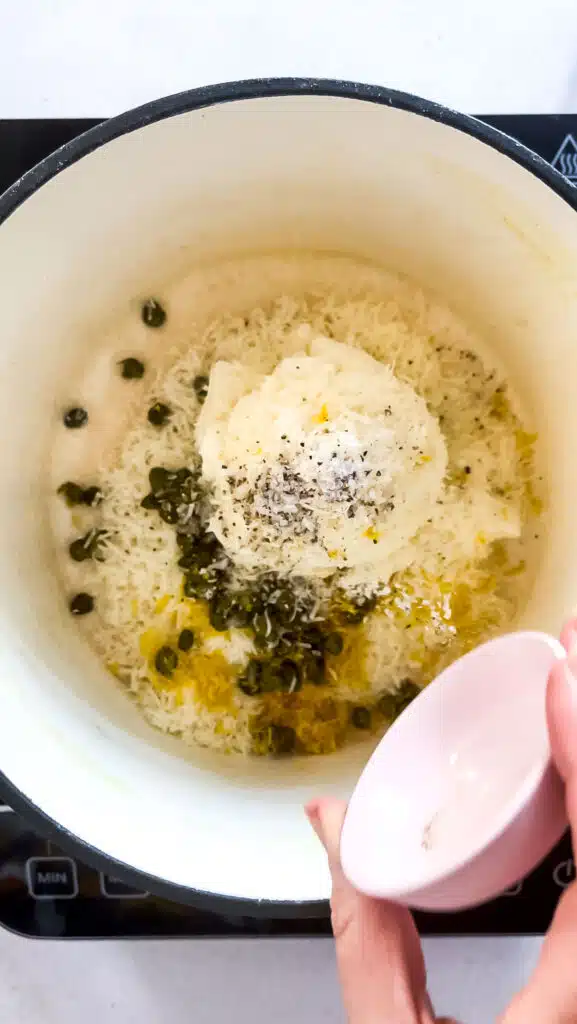 Ricotta, parmesan, lemon zest, capers, salt and pepper are being added to a pot to warm and make a sauce.