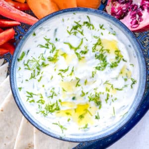 A square image showing a close up of tzatziki sauce in a bowl that has been drizzled with olive oil and sprinkled with dill.