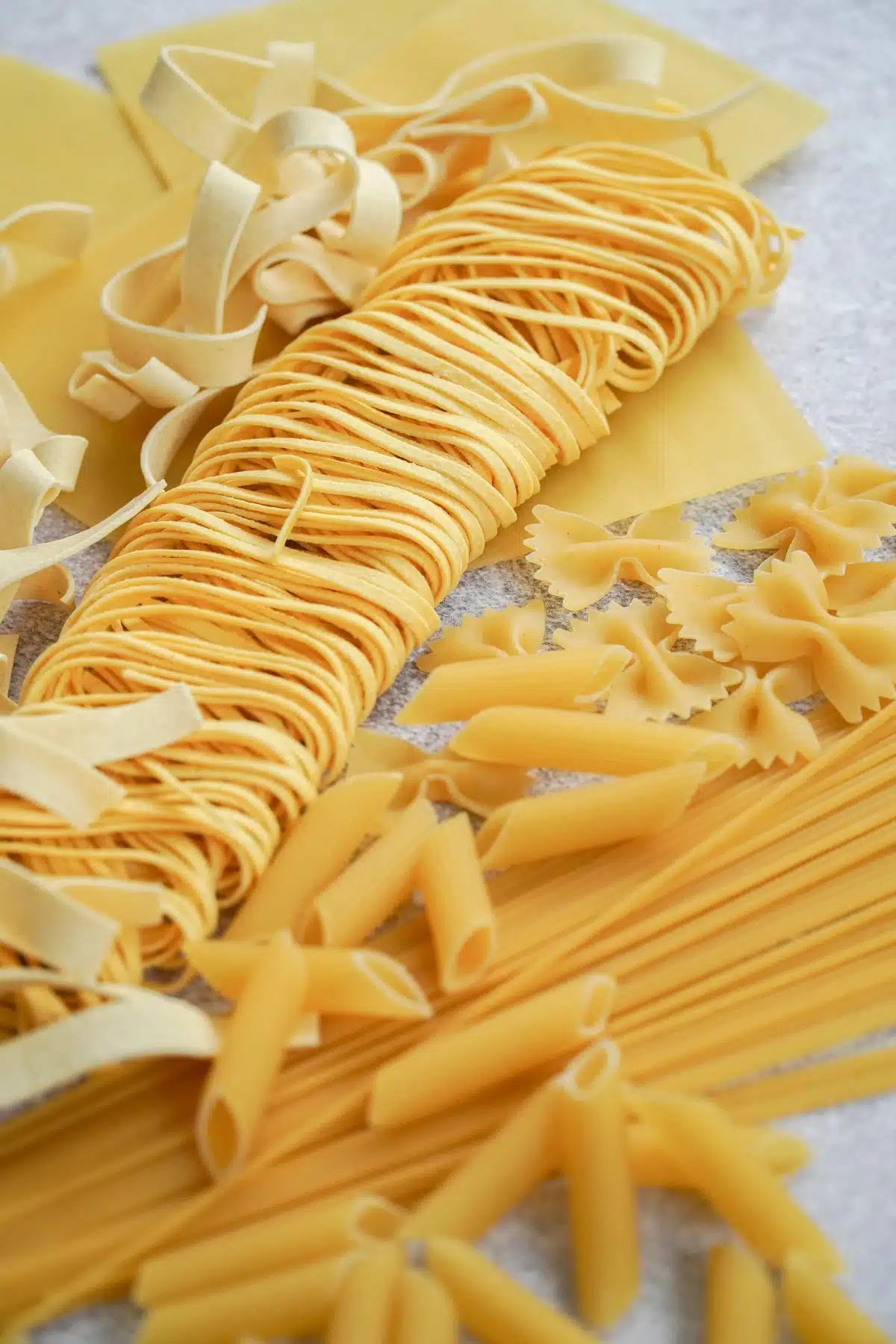 Various shapes of raw pasta have been laid out across a table.