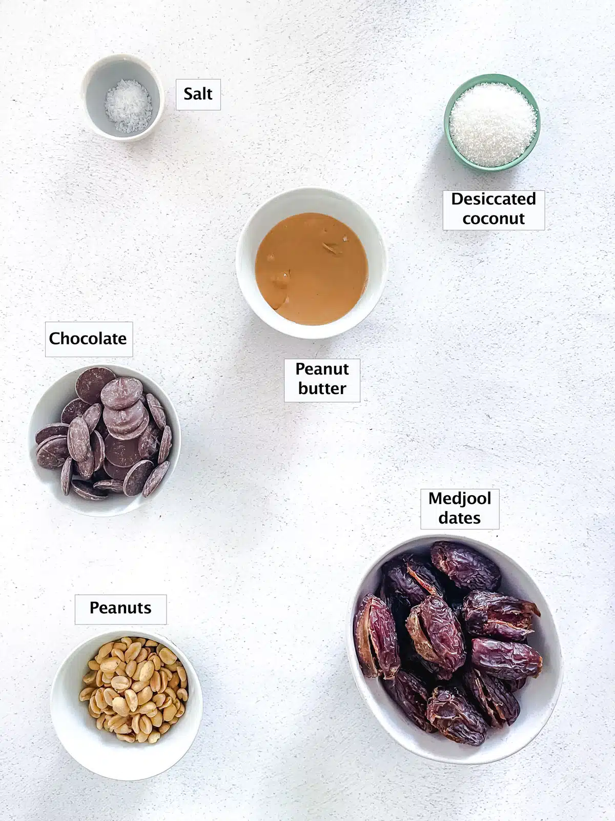 All the ingredients needed to make chocolate date bark have been laid out across a table in various small bowls.