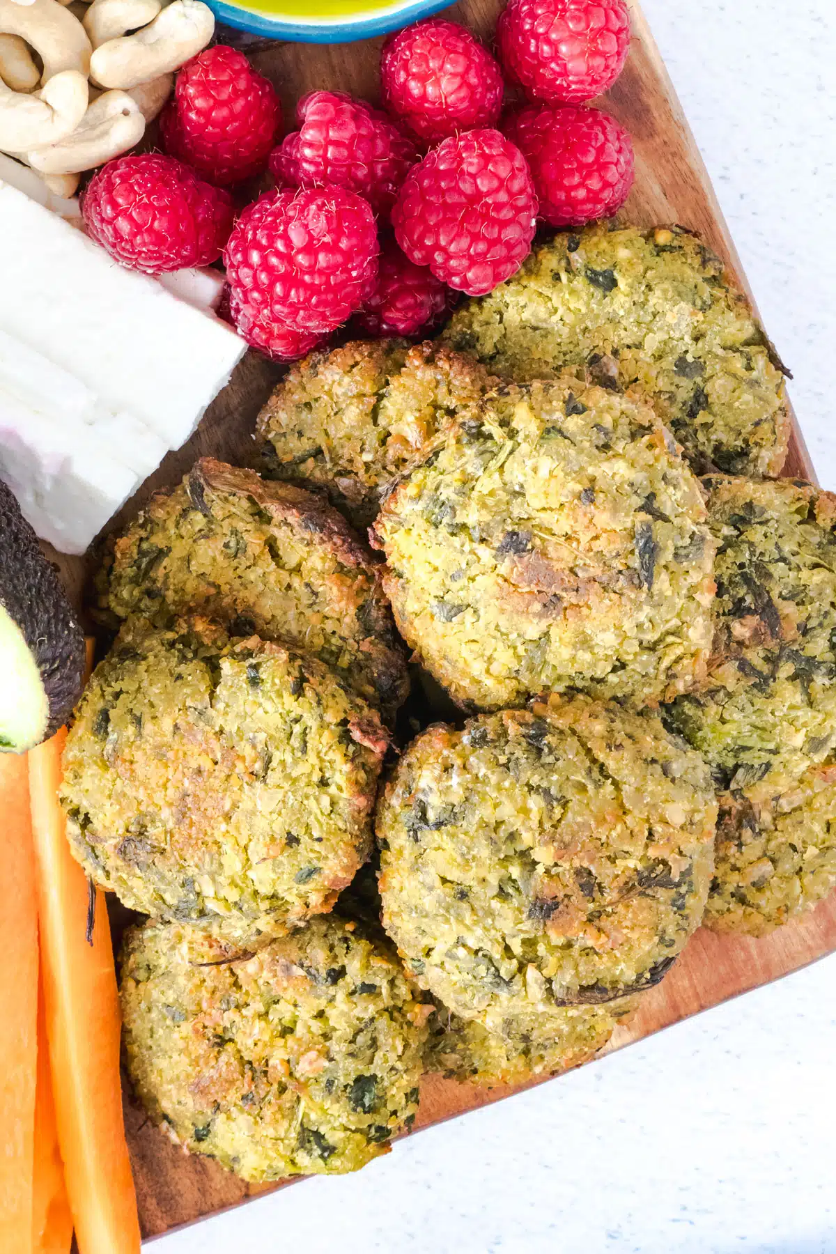 A close up of baked falafel on a mezze board. Carrots, raspberries, feta and cashews surround them.