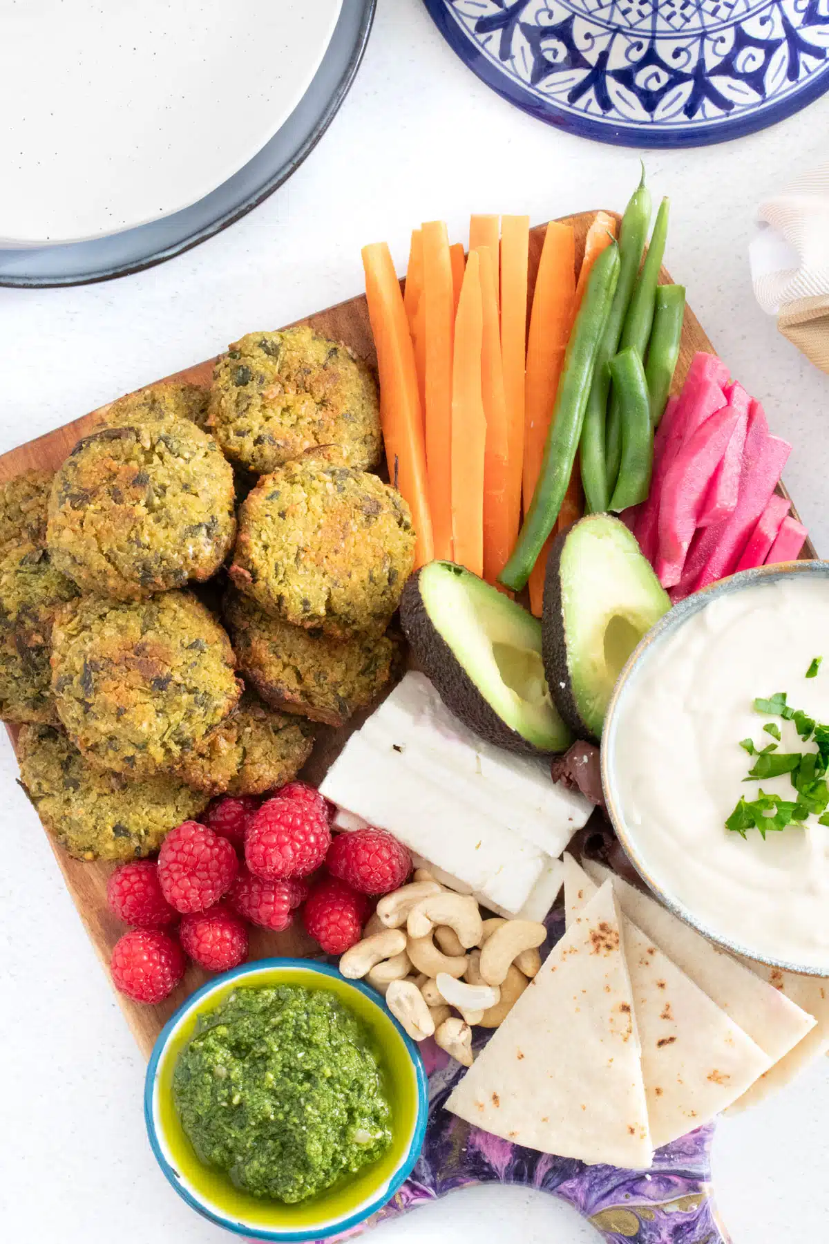 A mezze platter filled with baked falafel, berries, nuts, pita bread, dips, avocado, cut vegetables, pickles, and cheese.