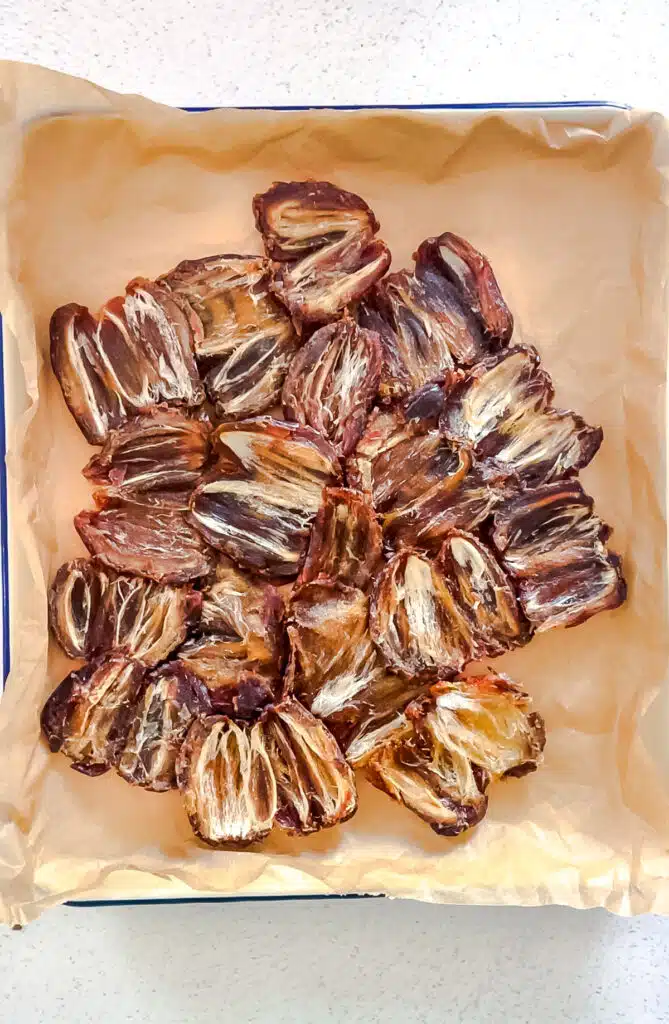 Deseeded dates have been spread out and flattened on a tray lined with baking paper - with the cut sides facing up.