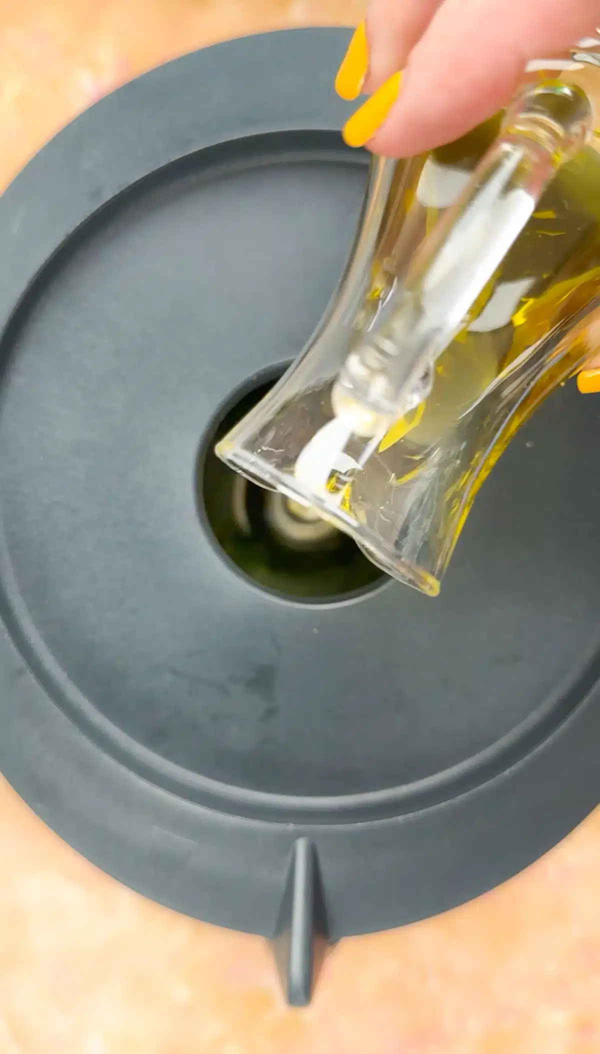 Olive oil is being drizzled through the opening in the lid of a food processor.