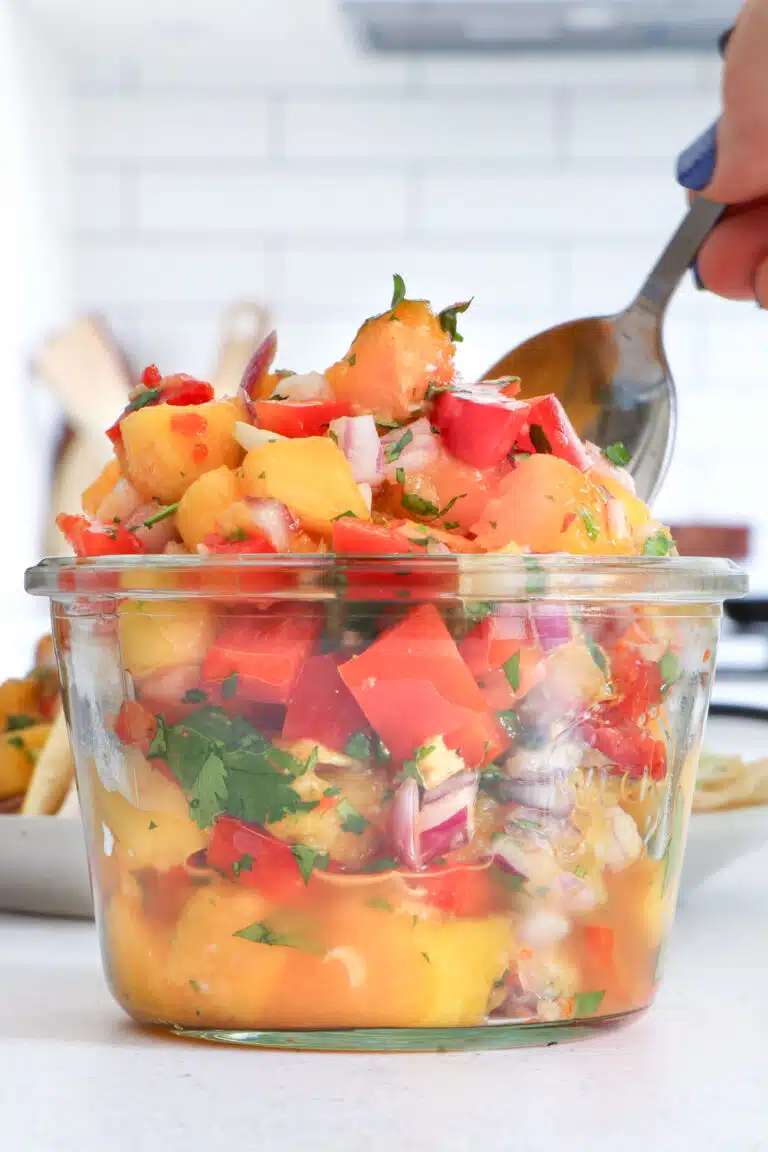 Looking straight at a jar of bright orange and red mango habanero salsa. A white hand is scooping some out with a spoon.