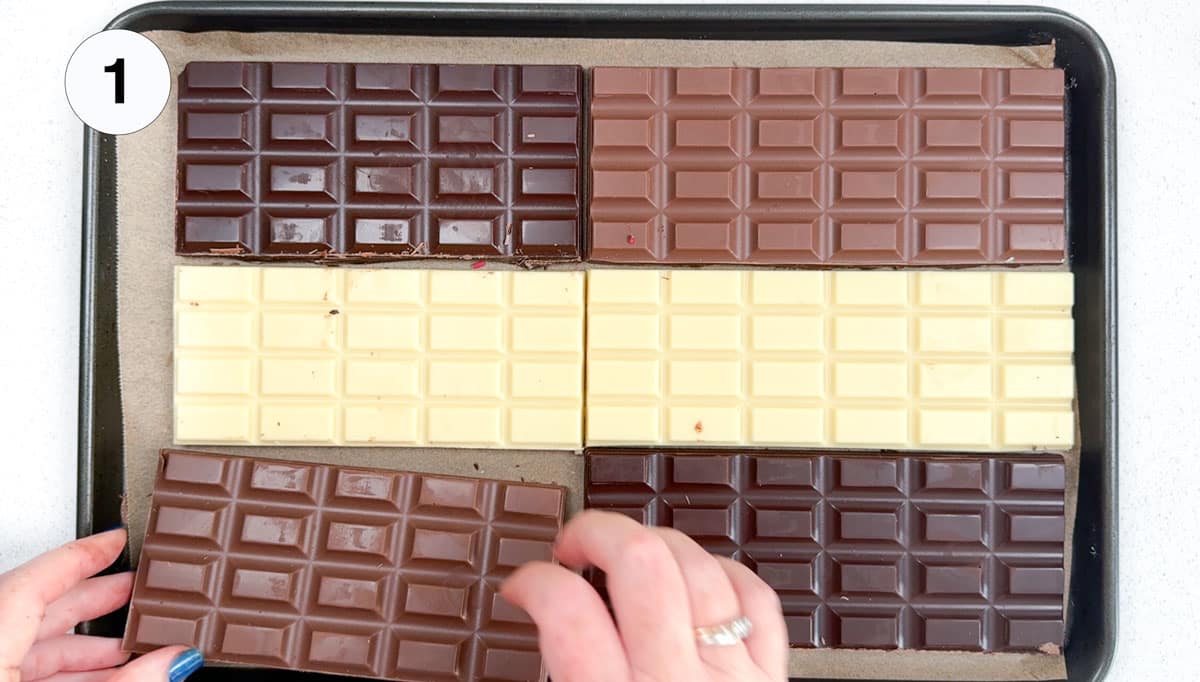 A white hand is laying out bars of dark, milk, and white chocolate on a baking tray.
