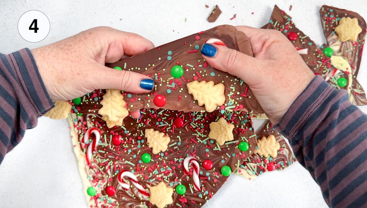Two white hands are holding a large piece of decorated chocolate bark and snapping it in half.