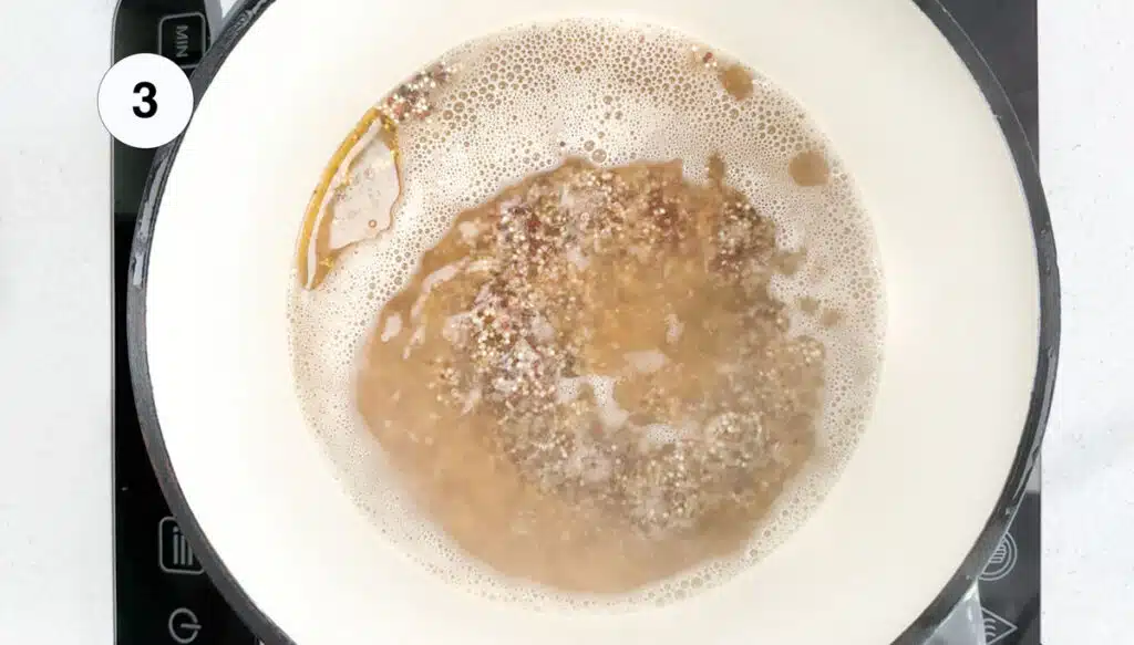 A pot of quinoa in chicken stock is boiling on the stove top.