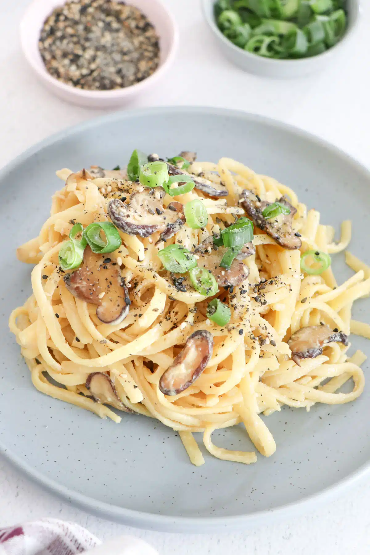 A grey plate has been piled with creamy miso pasta, topped with mushrooms, shallots, and gomasio.
