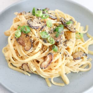 A close up of a pasta twirl with mushrooms, green onion and gomasio topping.