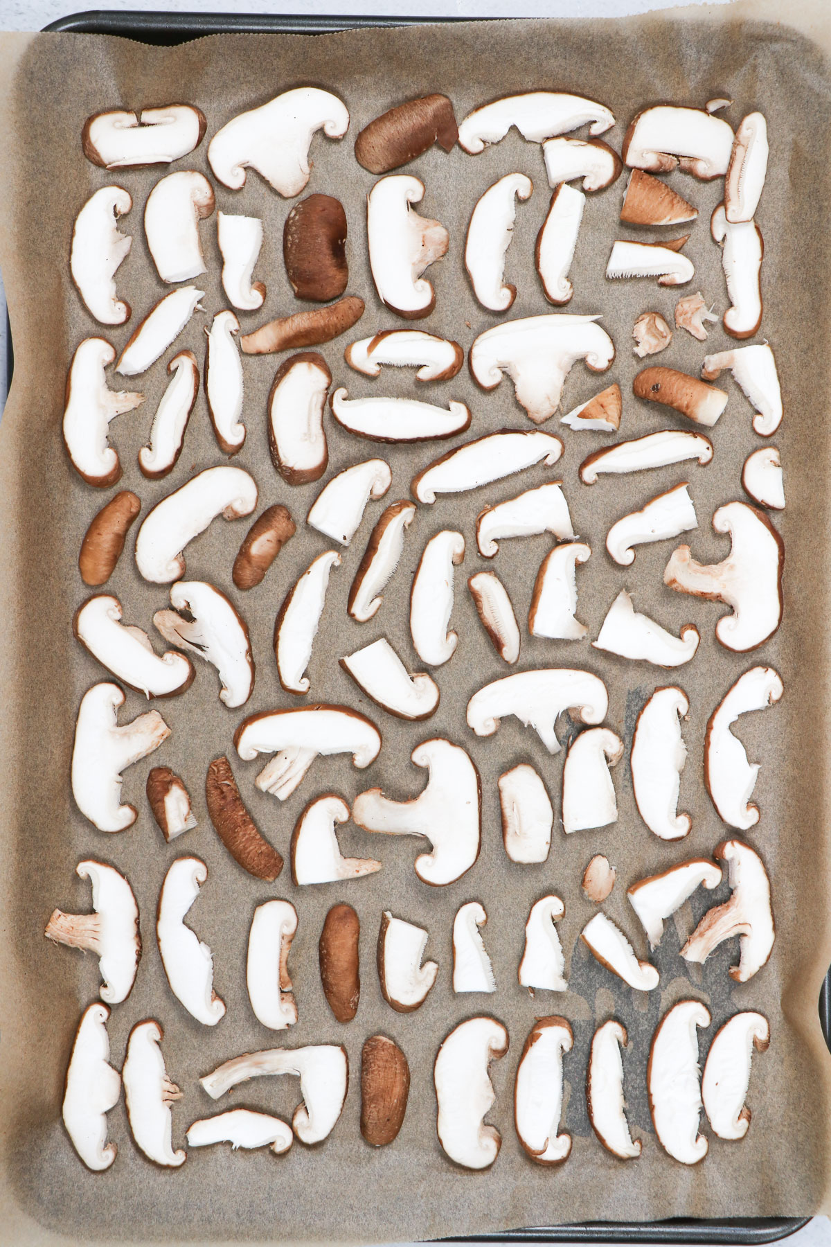 Mushroom slices have been laid out across a tray lined with brown baking paper.