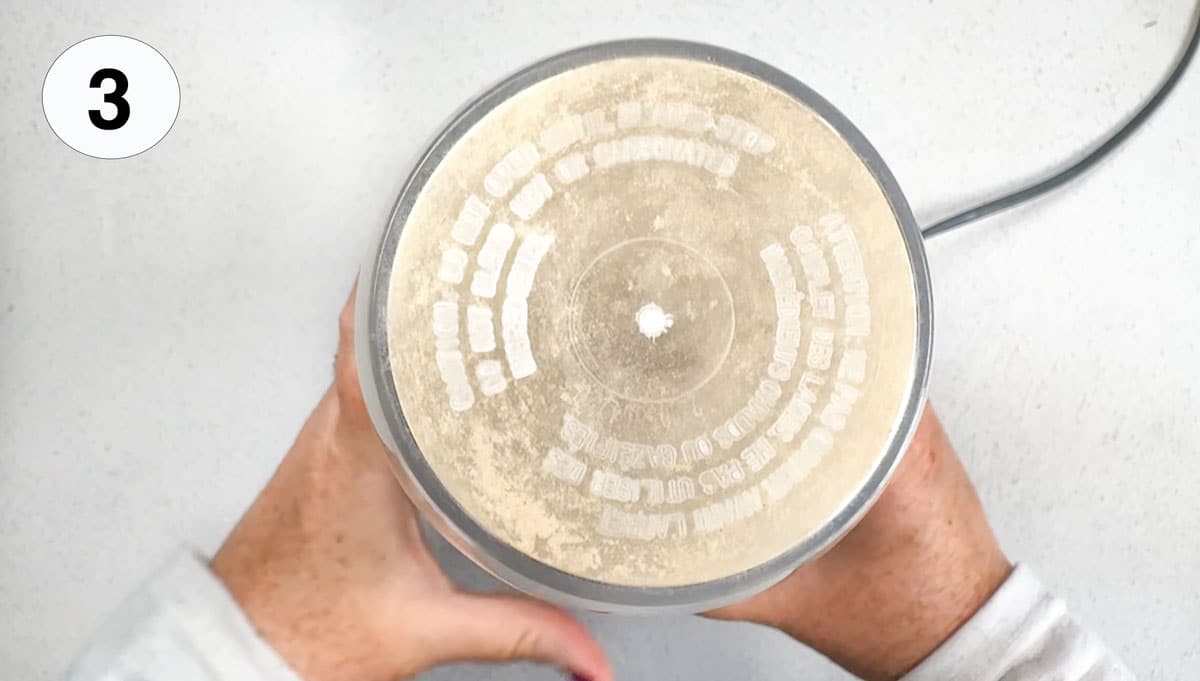 Two white hands are holding a nutribullet that is pulverising dried mushrooms into powder.