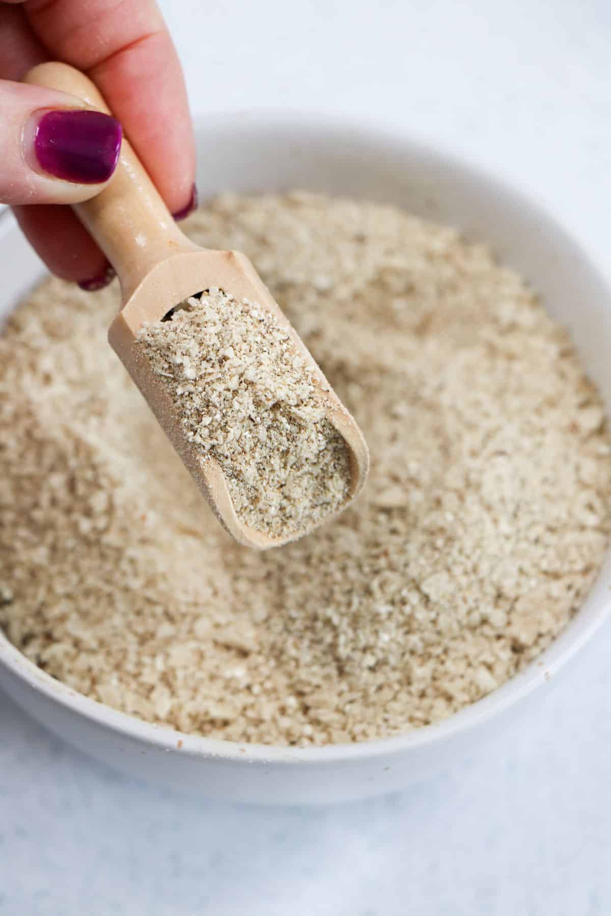 Mushroom salt is being removed from a small white bowl with a wooden scoop.